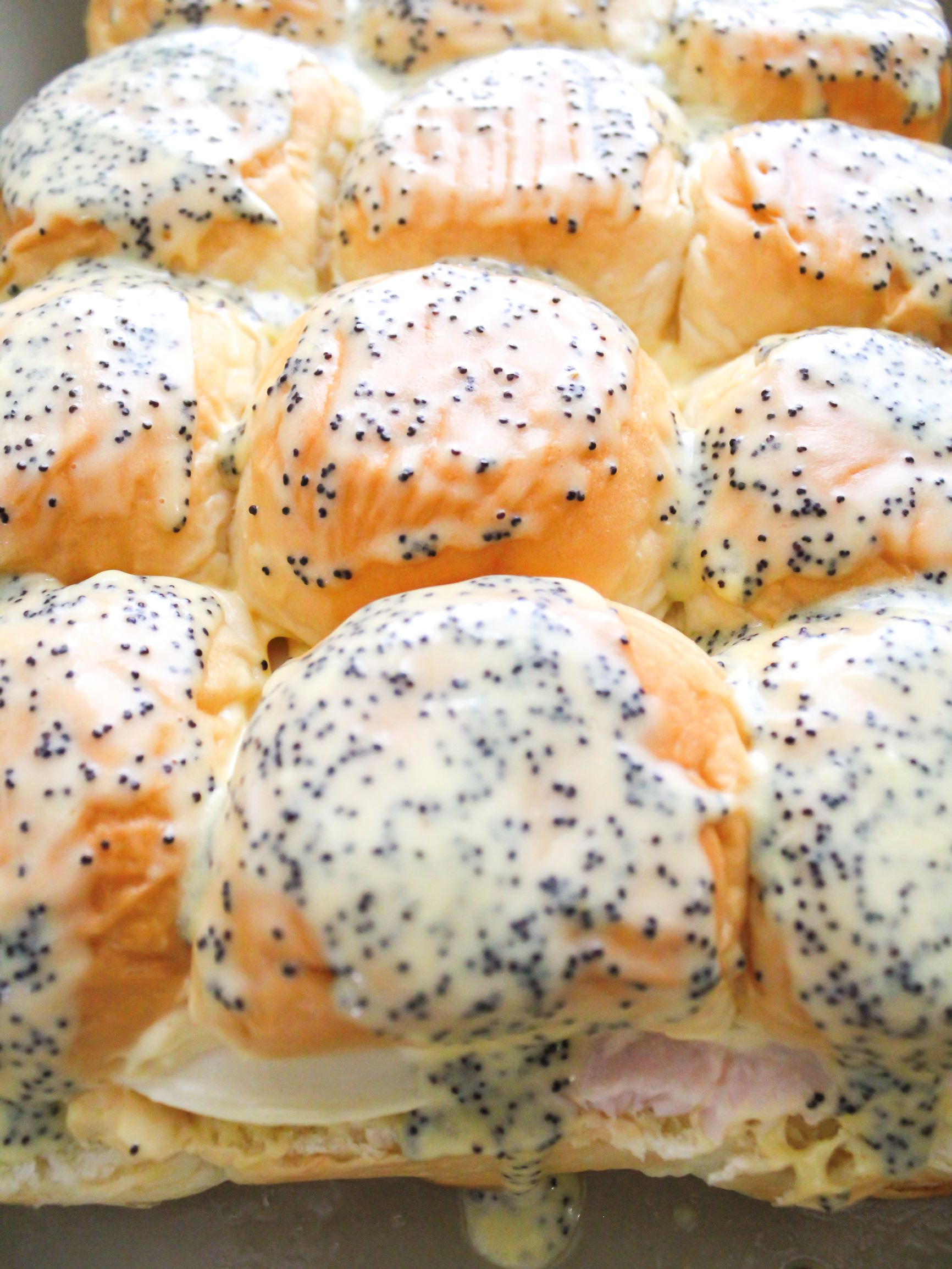 Slider sauce with poppy seeds brushed on top of turkey and provolone sliders