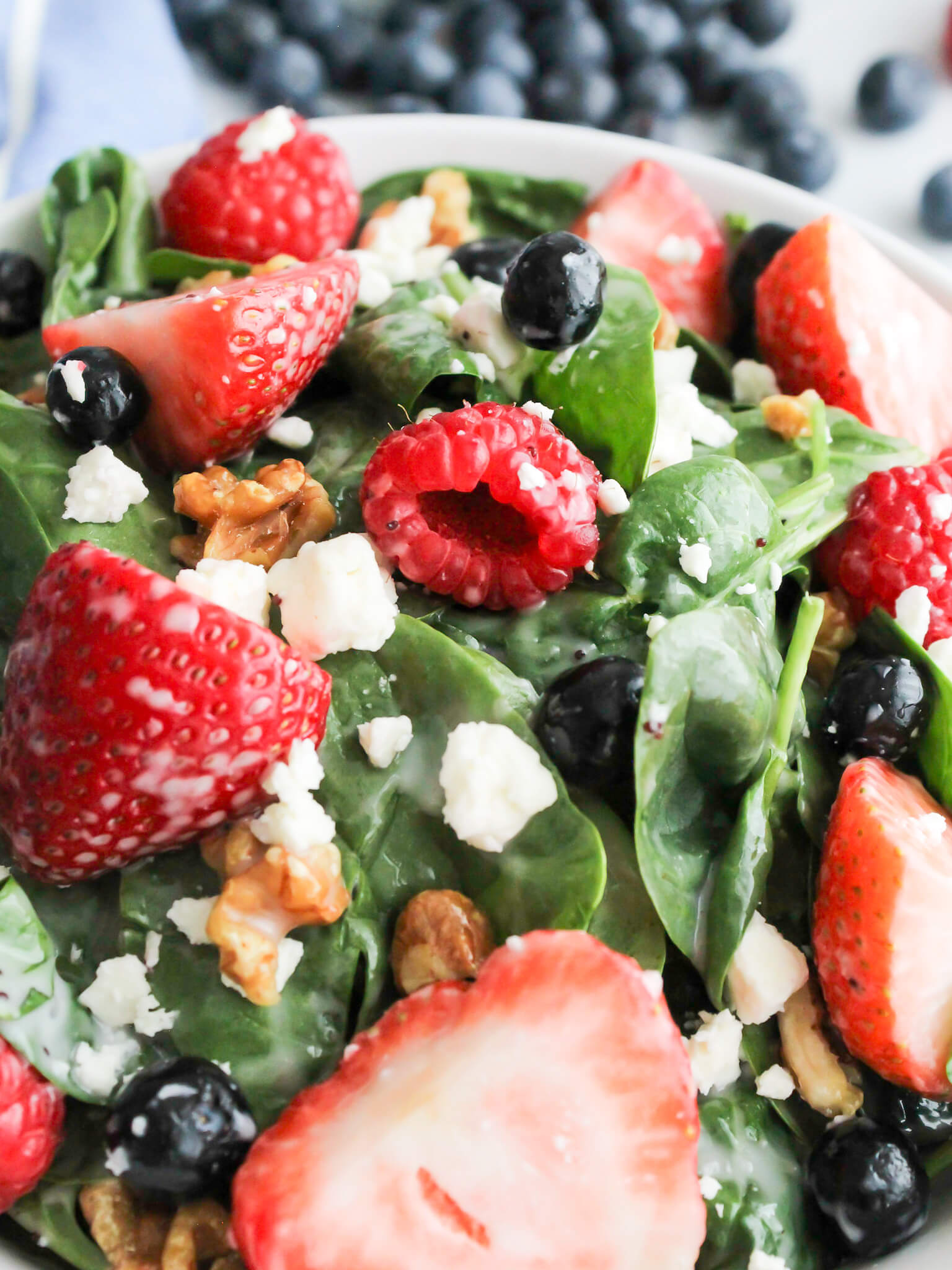 Close-up view of fresh raspberries, stawberries, blueberries, feta cheese, and walnuts on top of a bed of spinach