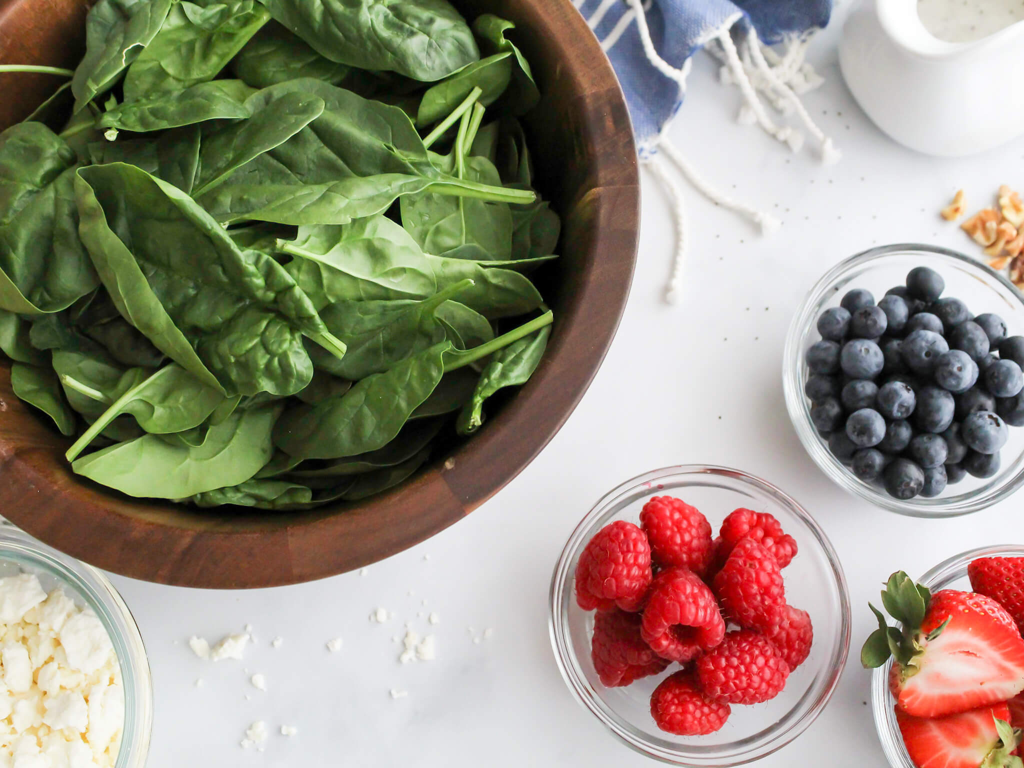 Ingredients to make summer salad including spinach in a wood serving bowl, fresh rasperies, blueberries, strawberries, chopped walnuts, and feta cheese