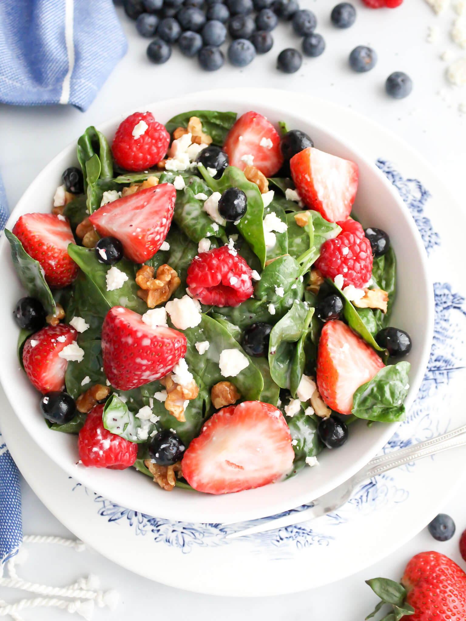Fresh spinach strawberry and bluberry salad with poppy seed dressing topped with feta cheese and walnuts