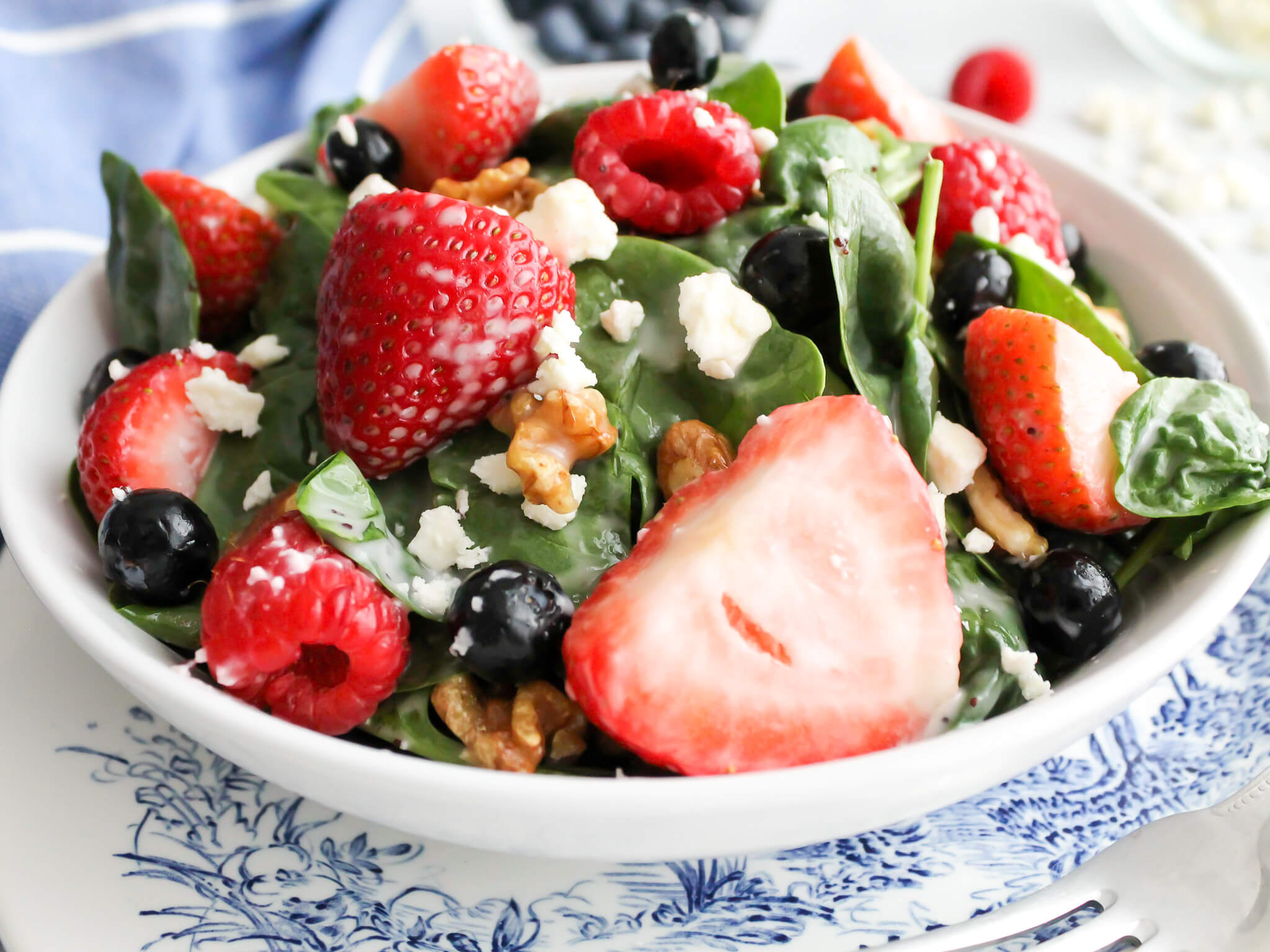 Horizontal view of bowl of fresh spinach strawberry and bluberry salad with poppy seed dressing topped with feta cheese and walnuts