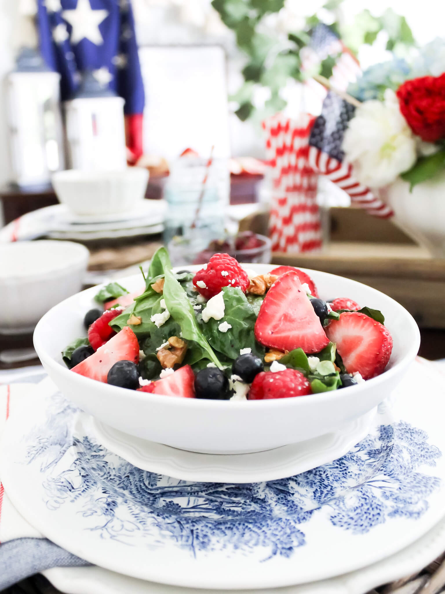 Spinach strawberry and bluberry salad served in a bowl placed on top of a blue and white transferware plate and placed on a table with 4th of July decorations