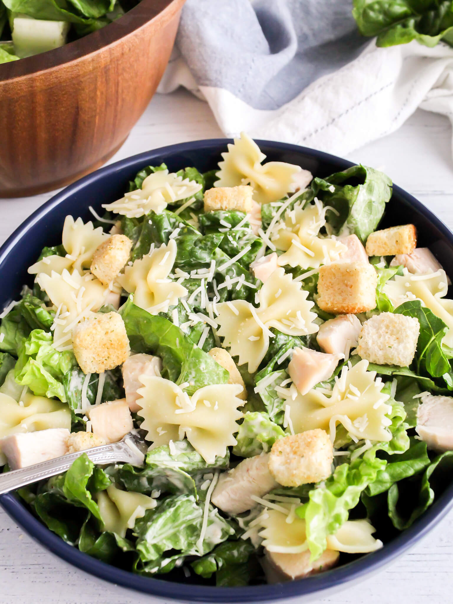 Bowtie chicken caesar salad garnished with fresh shredded parmesan cheese and crispy croutons