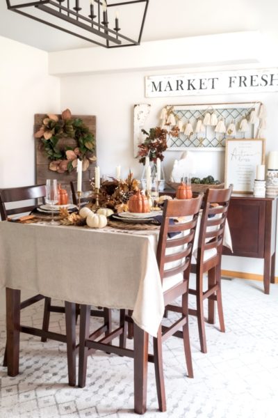 A farmhouse style dining room decorated for fall with the table set for a Friendsgiving brunch party including place settings, vintage brass candlesticks, mini white pumpkins, and a DIY cornucopia Thanksgiving centerpiece