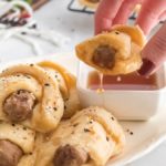 Hand holding a breakfast Sausage Crescent Roll with a bite taken out and dippedin maple syrup