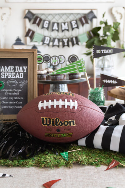 Centerpiece for a Super Bowl party tablescape with a football, chalkboard menu, pompoms, referee jersey, and free printable game day party pennants.
