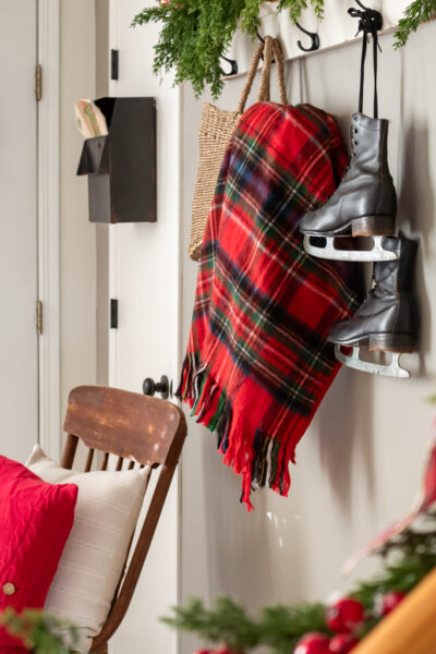 Vintage ice skates hanging beside a red and blue plaid blanket with Christmas greenery and red holiday accents.