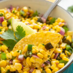 Bowl of chili roasted corn salsa with a yellow tortilla chip dipped in