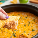 Hand dipping a tortilla chip into cheesy cream cheese bean dip