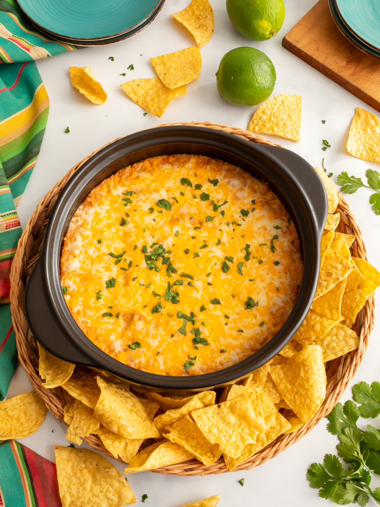 Baking dish with cream cheese bean dip and a wicker basket filled with tortilla chips