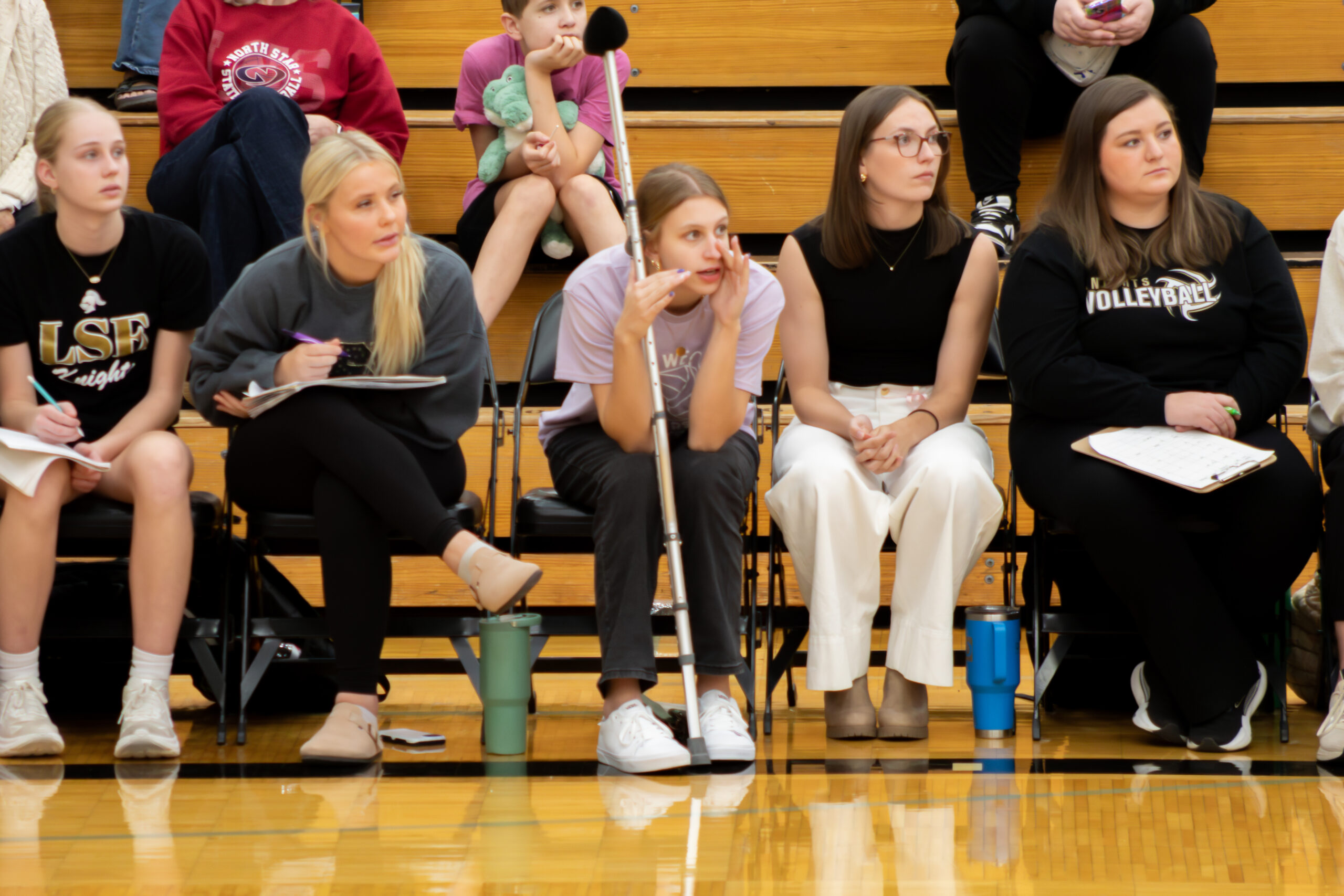 Injured volleyball player on the bench with crutch cheering for her team