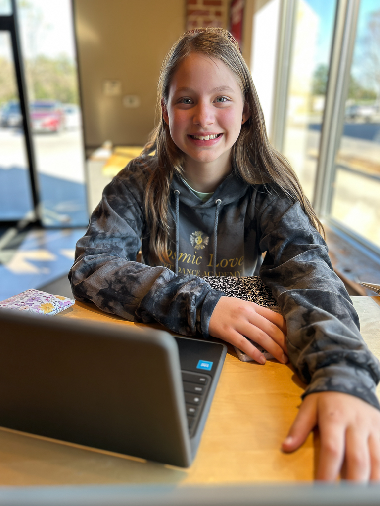 Girl smiling while doing homework on her computer in a coffee shop
