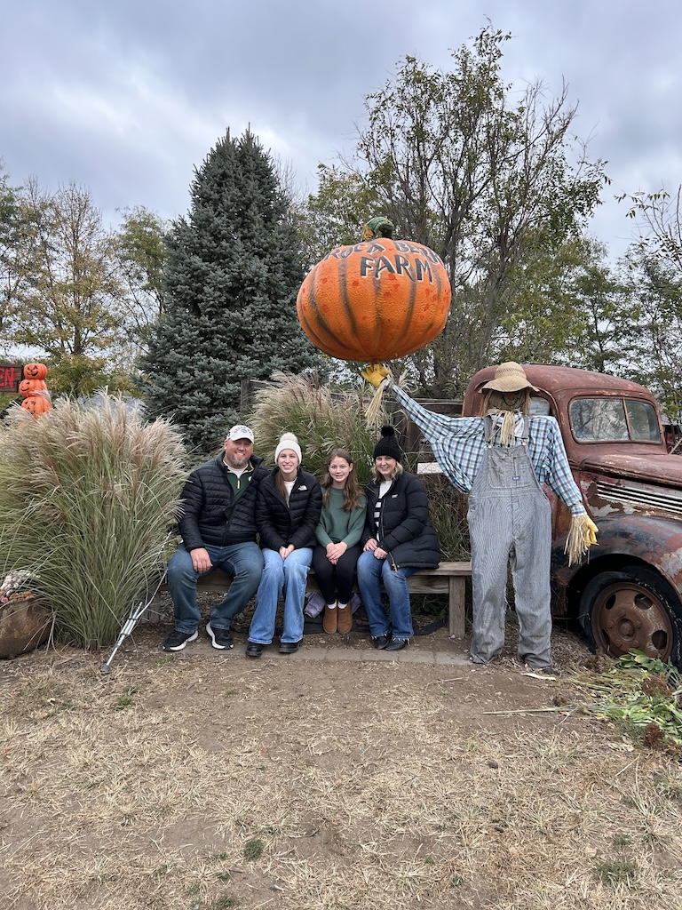 Family sitting on a bench and smiling in front of an old vintage truck at the pumpkin patch