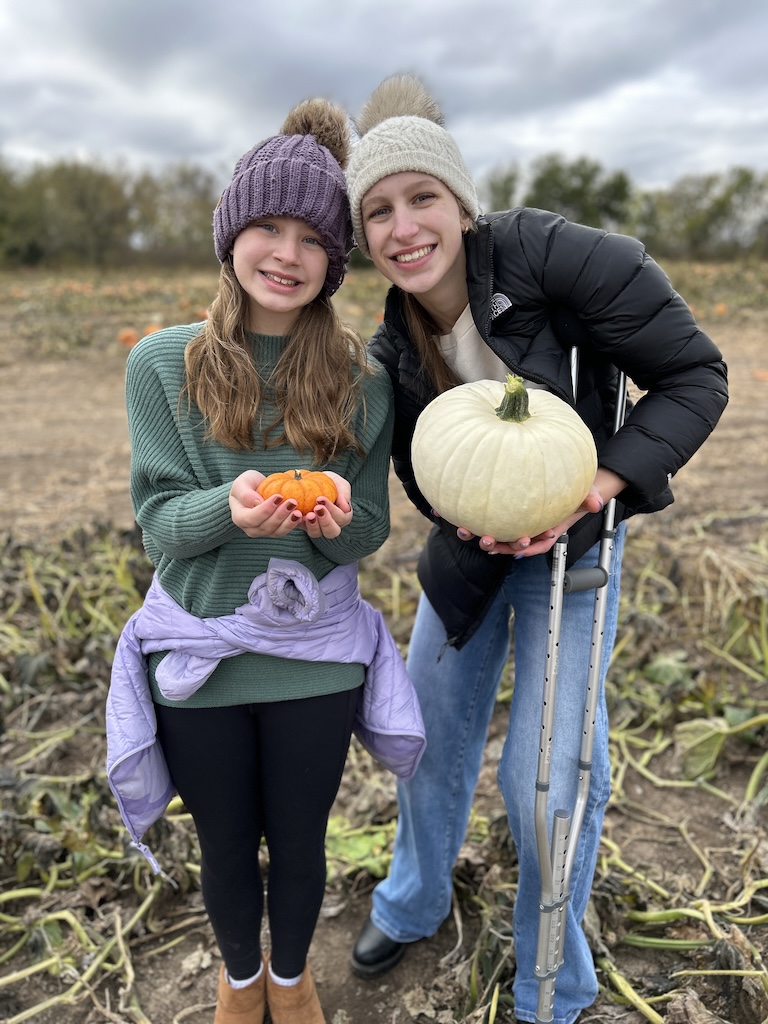 Girls smiling and hold pumpkins in a field at the pumpkin patch
