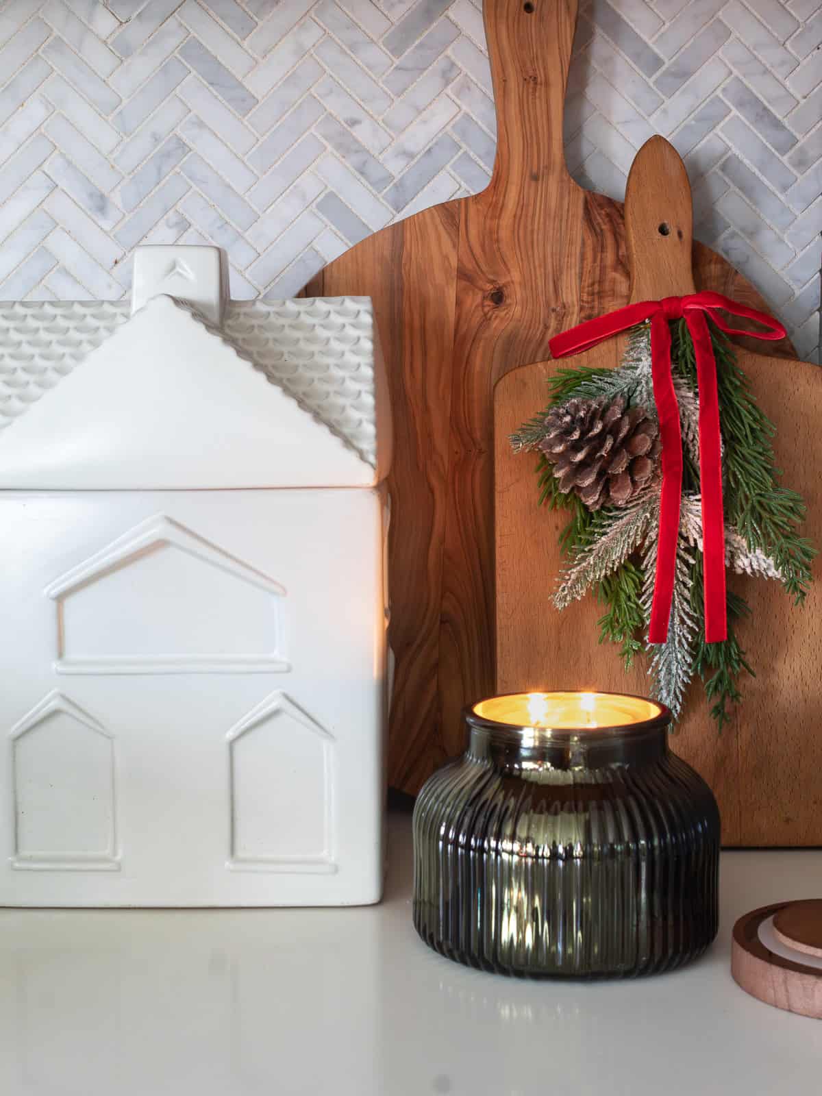 Cutting boards decorated for Christmas with greenery and red velevet ribbon along with a candle and white house cookie jar