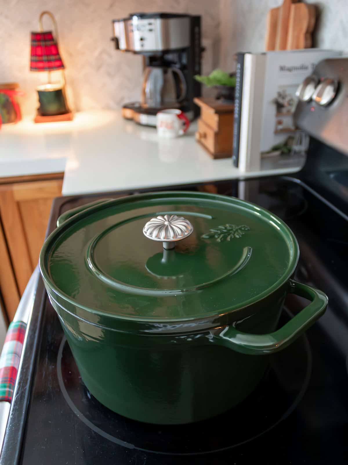 green pioneer woman dutch oven on the stovetop in the kitchen witha cofee maker, cookbooks, and plaid candle warmer in the background