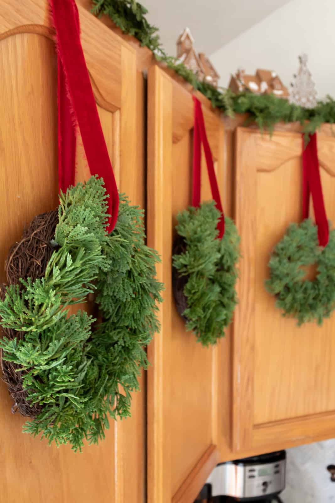 Small christmas wreaths hung on kitchen cabinets with red velvet ribbon