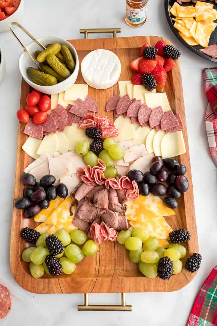 Building a Christmas tree charcuterie board with meat, cheeese, and fresh fruit