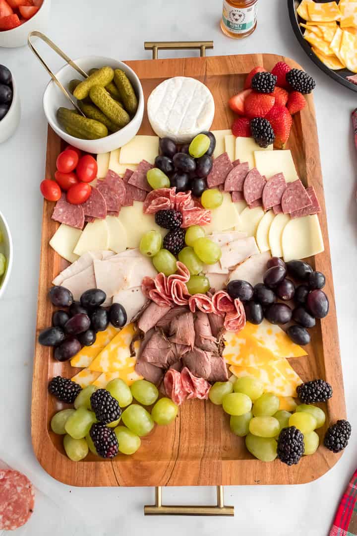 Christmas charcuterie board with meat, cheese, grapes, berries, crackers, honey and pickles