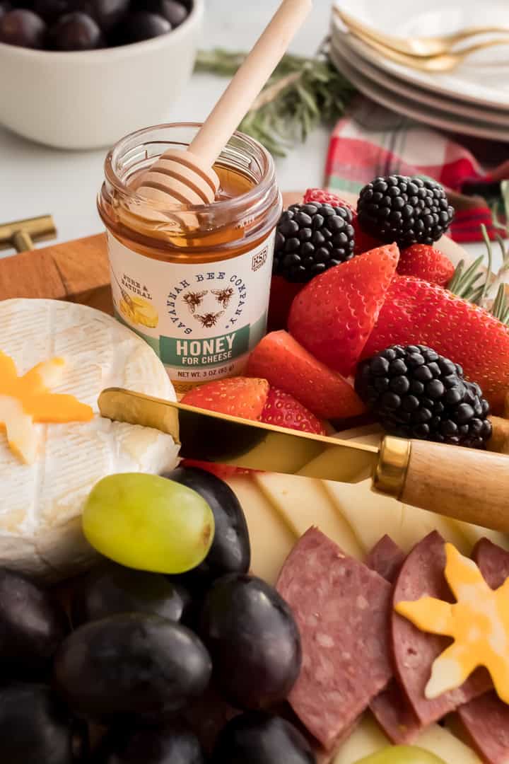 Close-up of a small jar of honey, brie, and fresh berries with meat and cheese on a Christmas charcuterie board