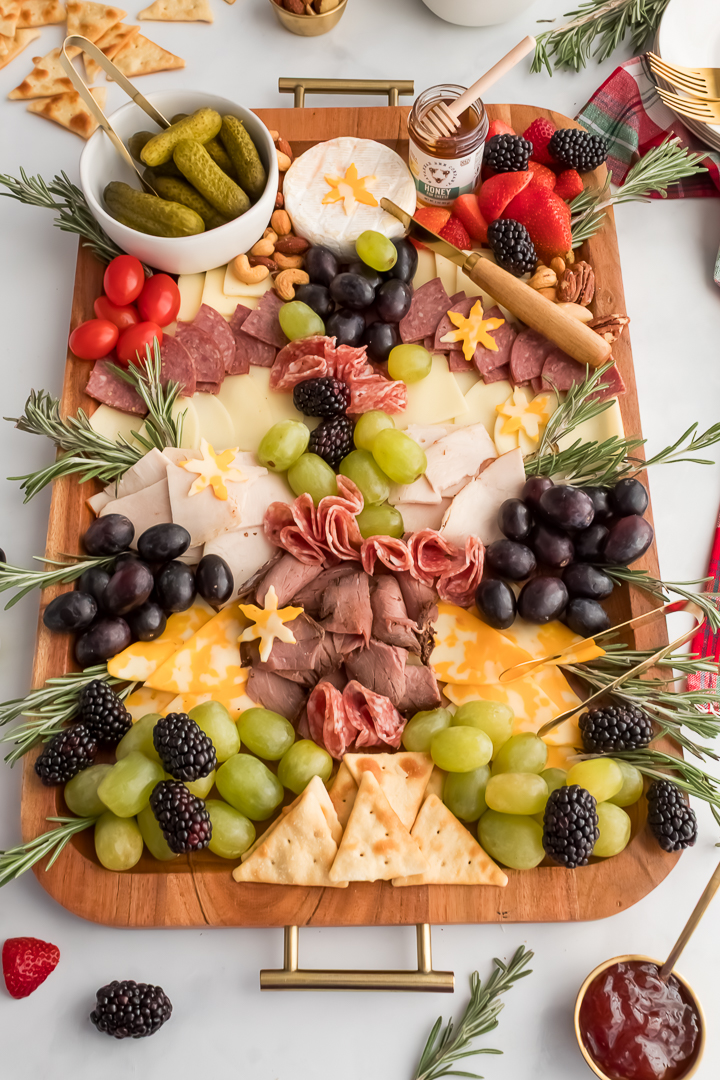 Overhead view of a Christmas tree Charcuterie board with meat, cheese, fresh berries, and garnished with fresh rosemary