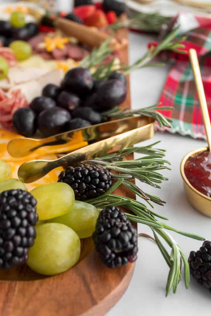 Close-up of rosemary garnish with fresh fruit and mini gold serving tongs on a Christmas charcuterie board