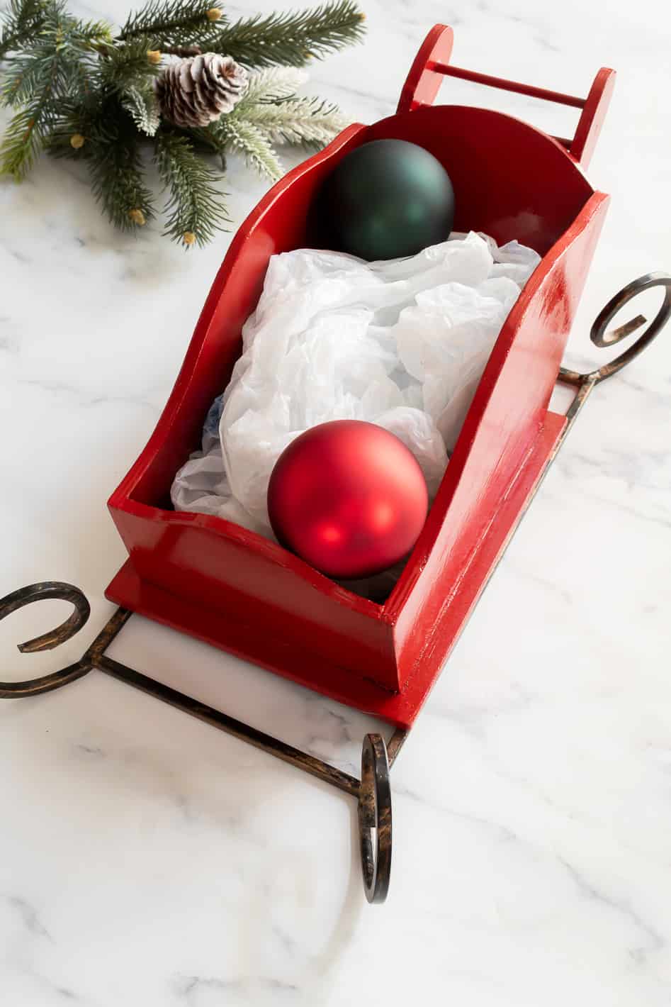 Adding Christmas ornaments to a wooden sleigh to make a holiday centerpiece