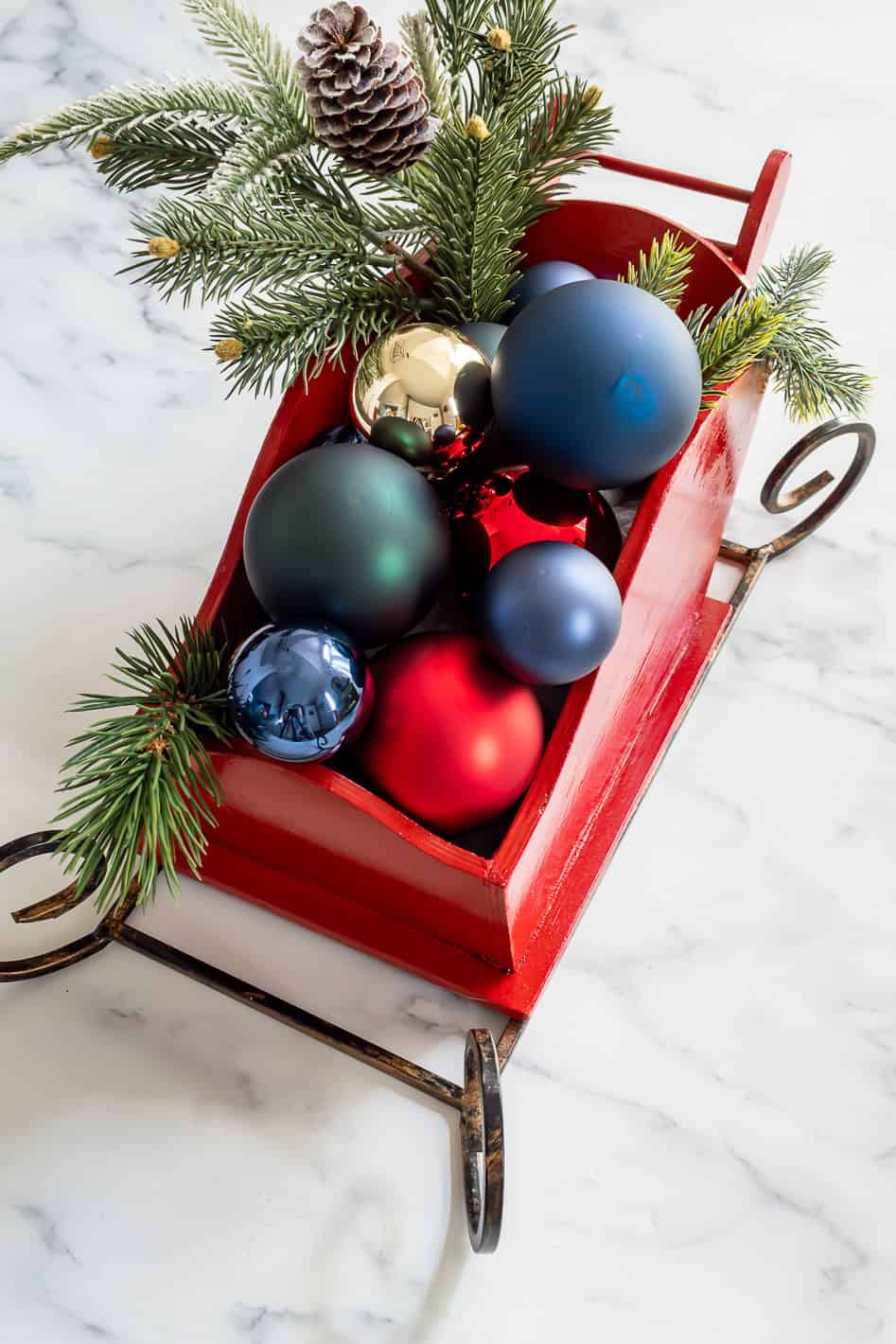 Overhead view of faux greenery and red, gold, blue and green ornaments inside of wood sleigh Christmas centerpiece