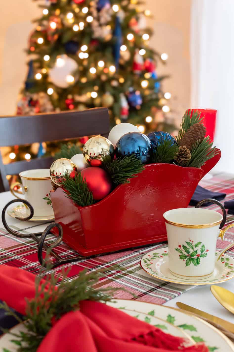 Close up view of wooden red DIY Christmas sleigh centerpiece styled on a dining rom table filled with red, gold, white and blue ornaments and faux greenery