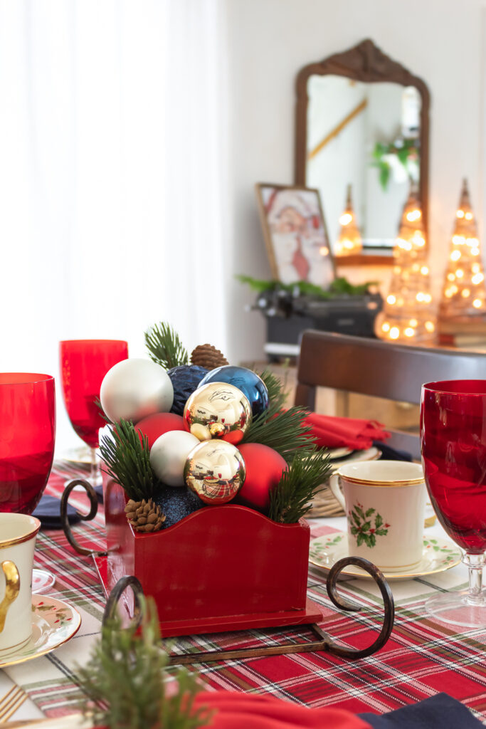 Close up view of wooden red DIY Christmas sleigh centerpiece styled on a dining rom table filled with red, gold, white and blue ornaments and faux greenery