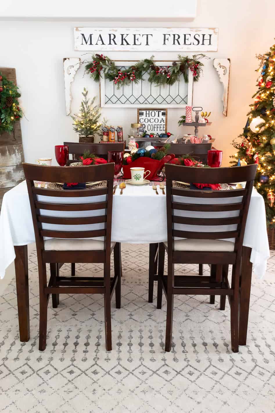 Full view of farmhouse style dining room decorated for Christmas in traditional red and blue colors with the table set for Christmas dinner including a DIY Christmas sleigh centerpiece