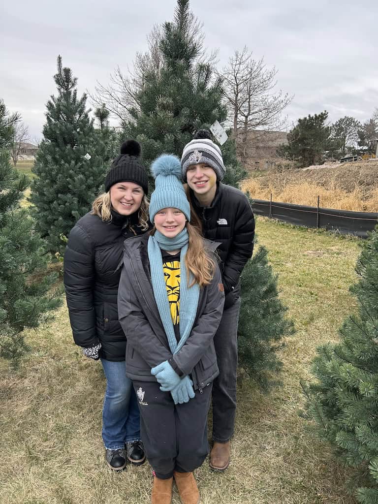 girls and mom smiling and posing at a Christmas tree famr