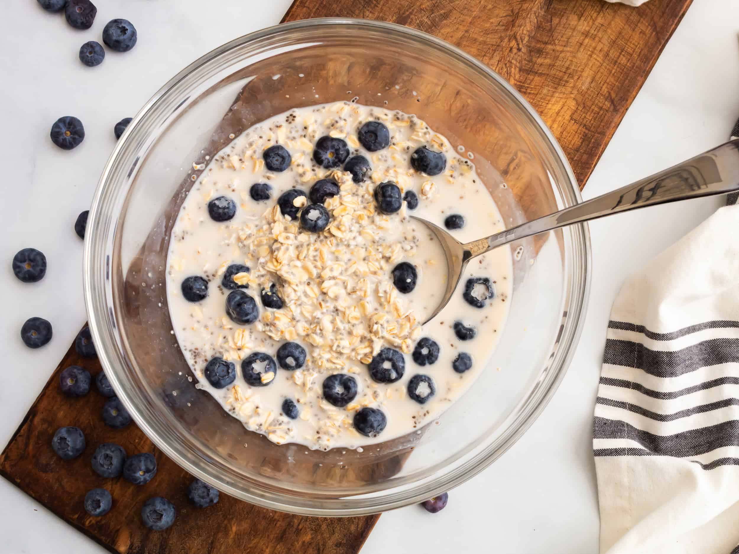 A spoon lifting a scoop of blueberry overnight oats from a glass bowl, showing the creamy oat mixture and juicy blueberries.
