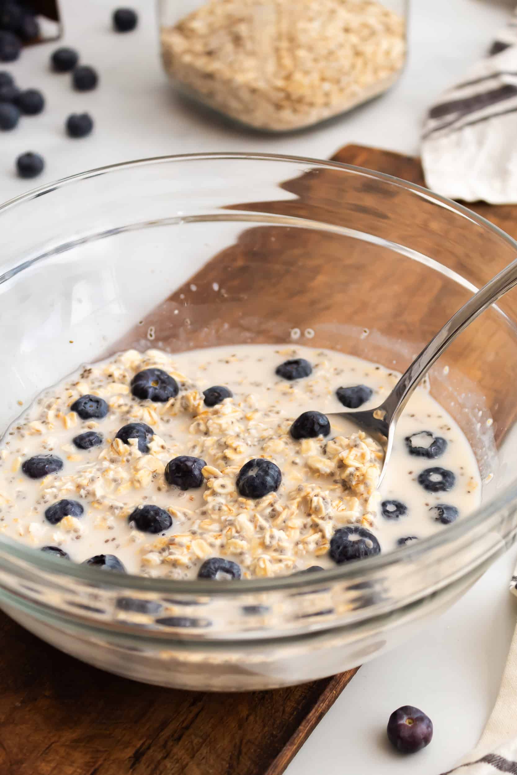 Close up of blueberry overnight oats in a glass bowl with a spoon resting inside, highlighting the texture of the oats and fresh blueberries.