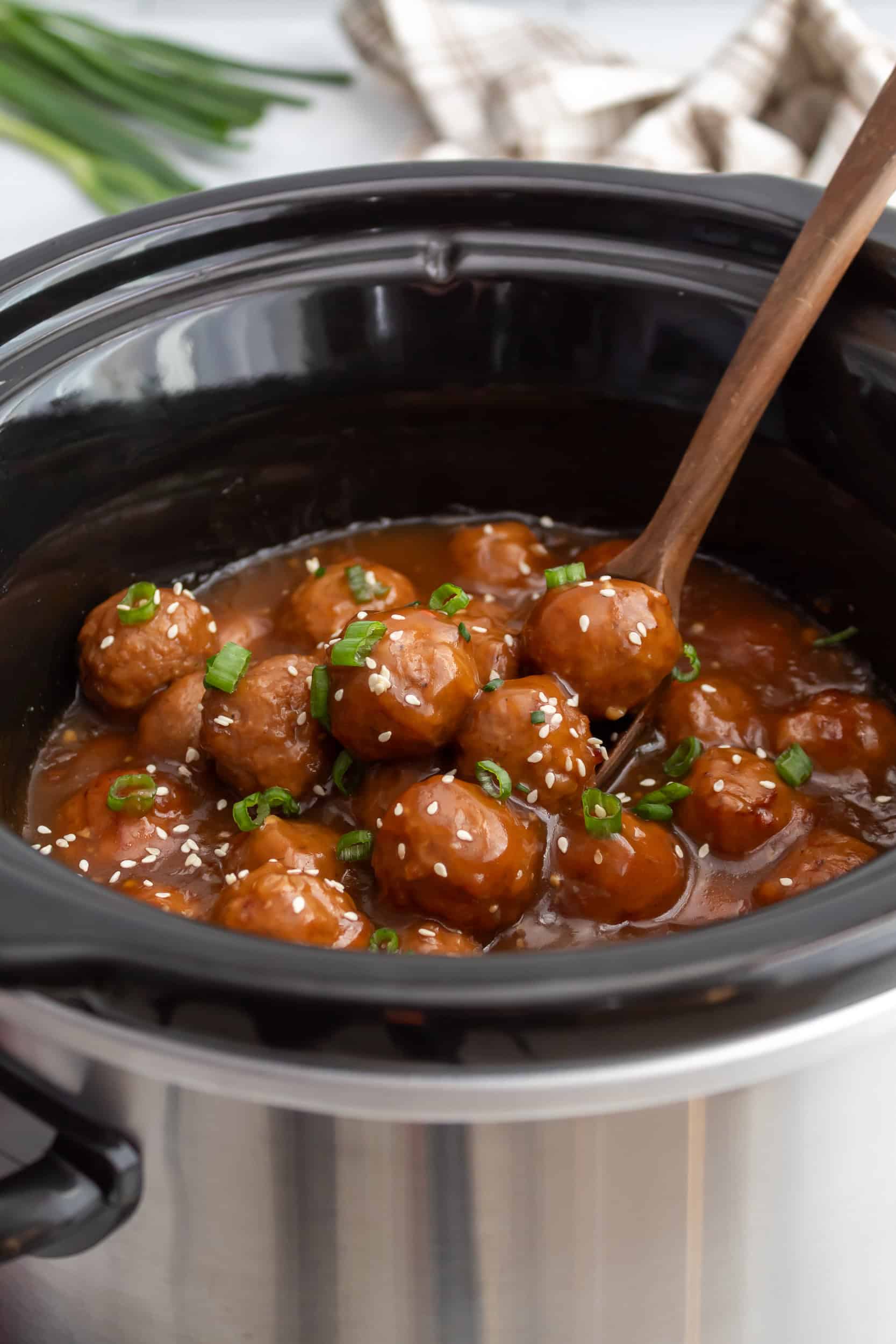 Crockpot teriyaki meatballs simmering in a slow cooker with sauce, garnished with sliced green scallions and sesame seeds.