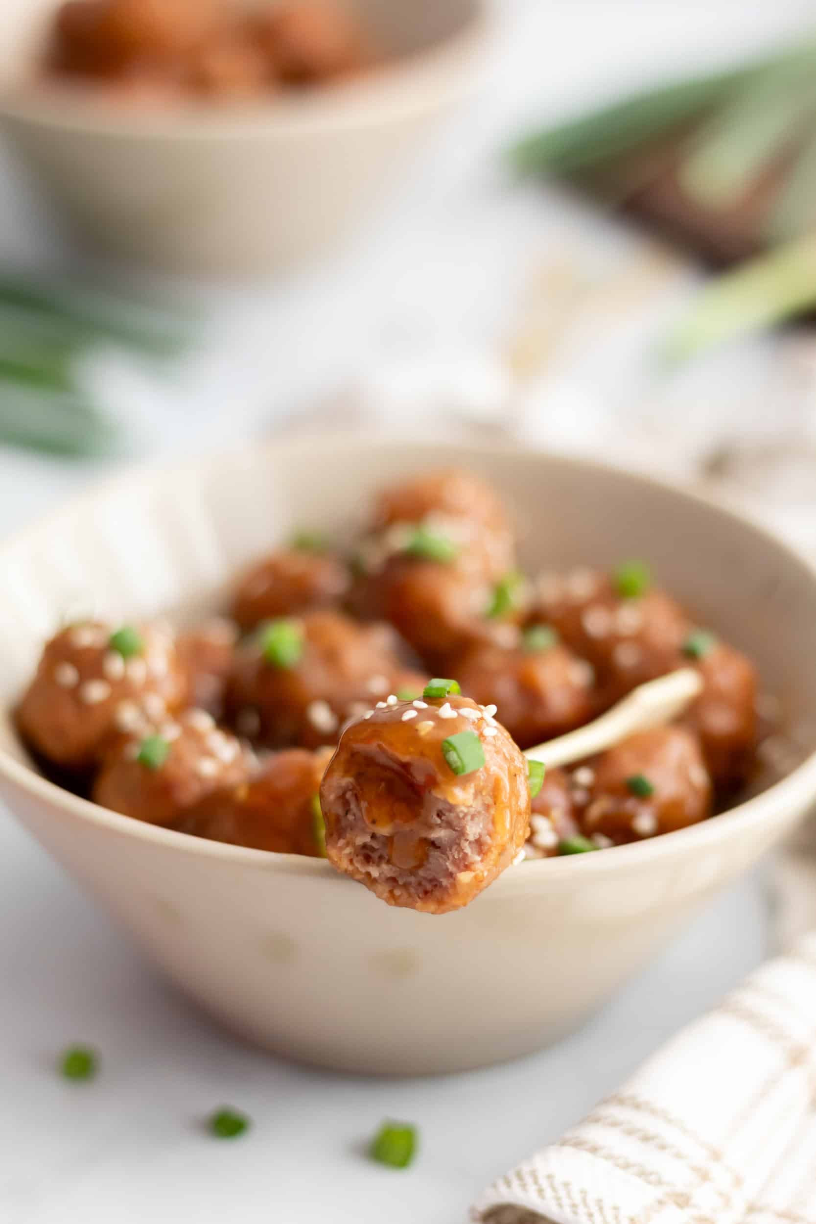 A single crockpot teriyaki meatball held on a toothpick, showing the tender inside and sticky teriyaki glaze.