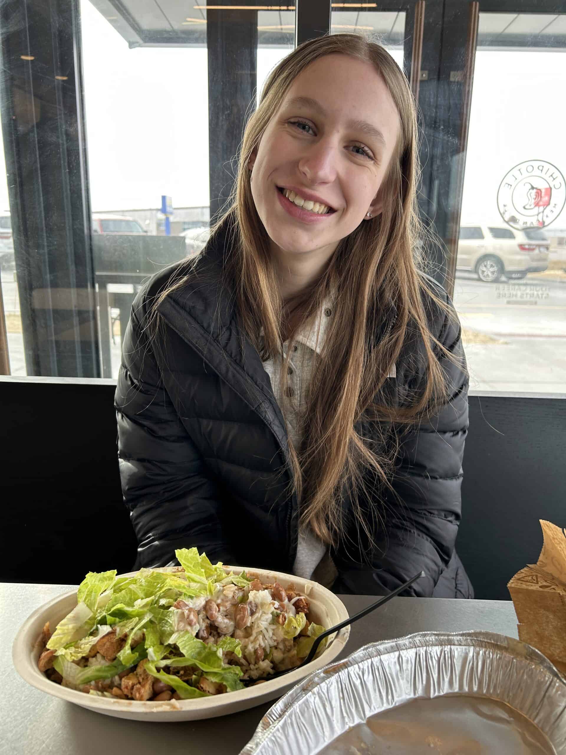 girl smiling at lunch sitting down to eat a Chipotle burrito bowl