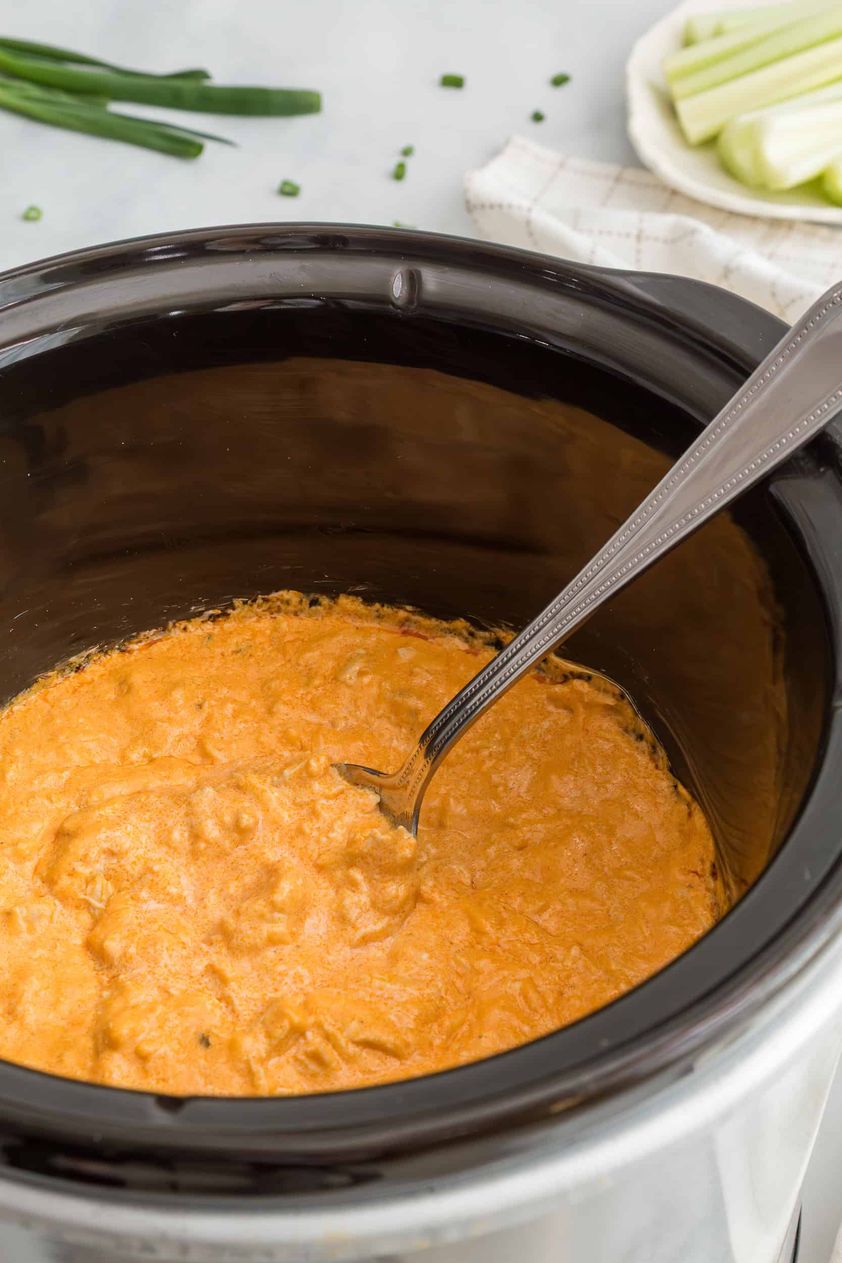 Crockpot buffalo chicken dip finished and creamy inside a slow cooker with a serving spoon