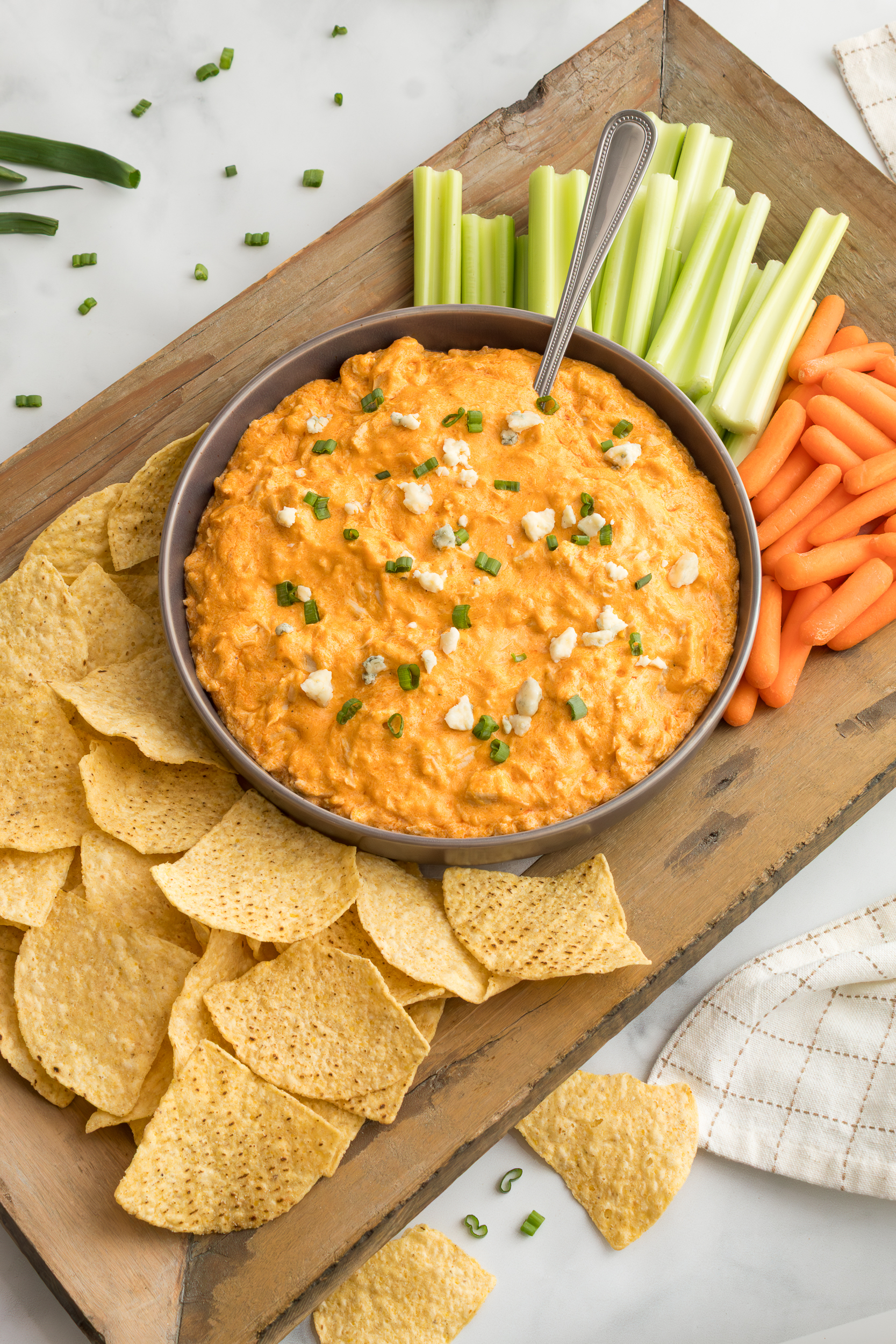 Crockpot buffalo chicken dip on a wooden board surrounded by tortilla chips and fresh vegetables
