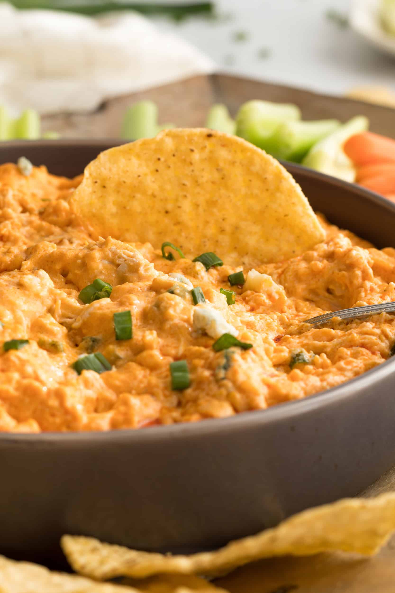 Tortilla chip dipping into crockpot buffalo chicken dip topped with green onions