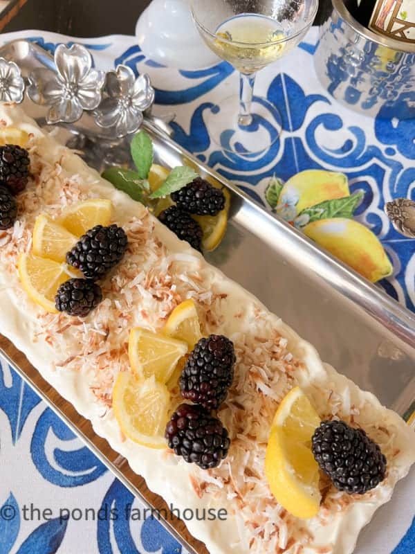 Overhead view of tray with frozen limoncella dessert topped with toasted coconut, fresh blackberries and garnished with lemon wedges and mint for an Italian dinner party menu.