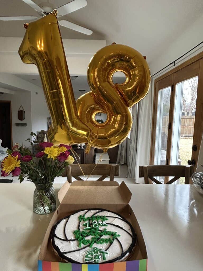 gold 18 birthday balloons, bouquet of colorful flowers and a cookie cake sitting on the kitchen counter