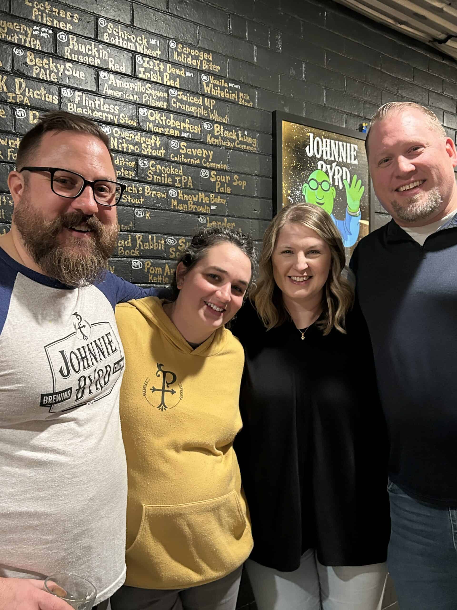 2 couples standing and smiling for a photo at a brewery for a 40th birthday suprise party