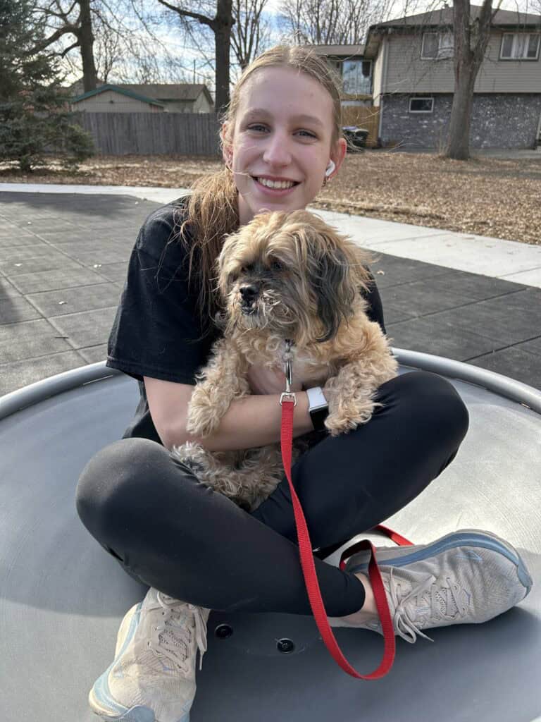 Girls sitting on playground equipment at the park smiling and holiding a small dog