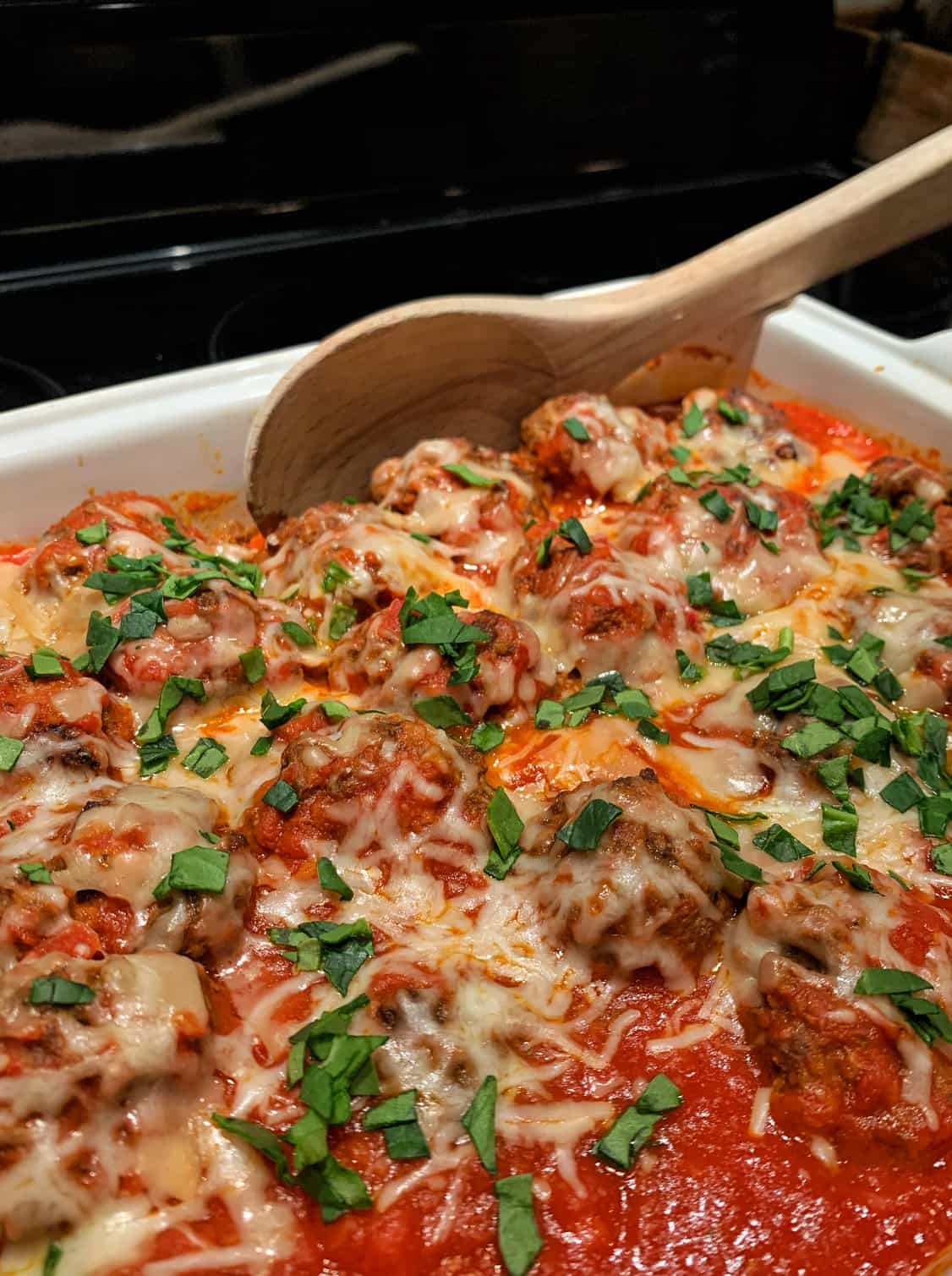 Close up view of Italian oven baked meatballs smothered in a tomato-based Sunday sauce and garnisehd with fresh parsley. A main course for an Italian dinner party menu.