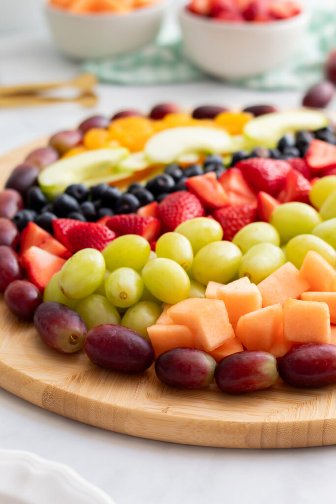 Full angled view of a colorful Easter egg fruit charcuterie board with rows of cantaloupe, green grapes, strawberries, blueberries, green apple slices, and mandarin oranges outlined with red grapes