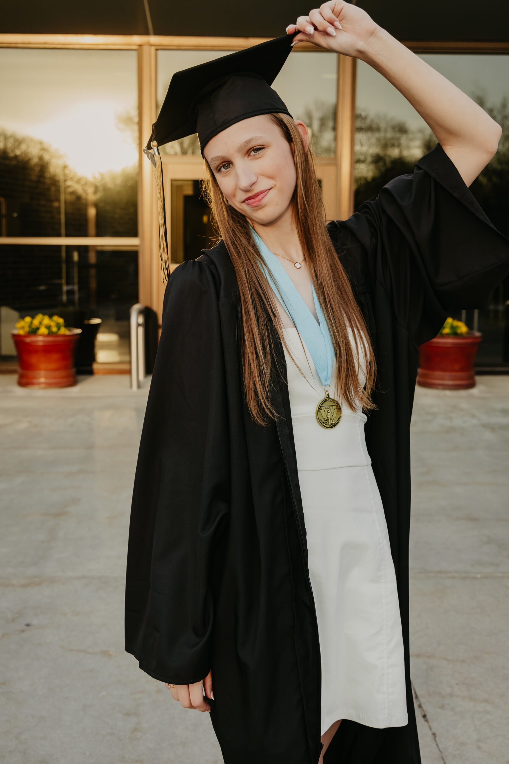 Girl smiling for high school graduation cap and gown photos in her gown and holding the tip of her cap
