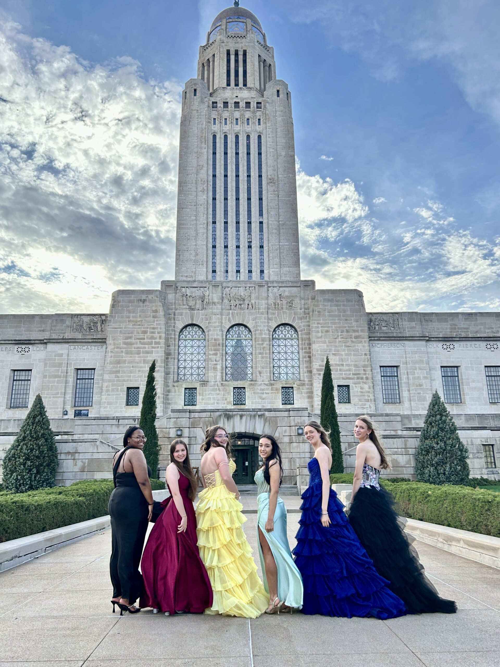 Friends in colorful prom dresses standing and posing in front of the Nebrasks state capitol for photos