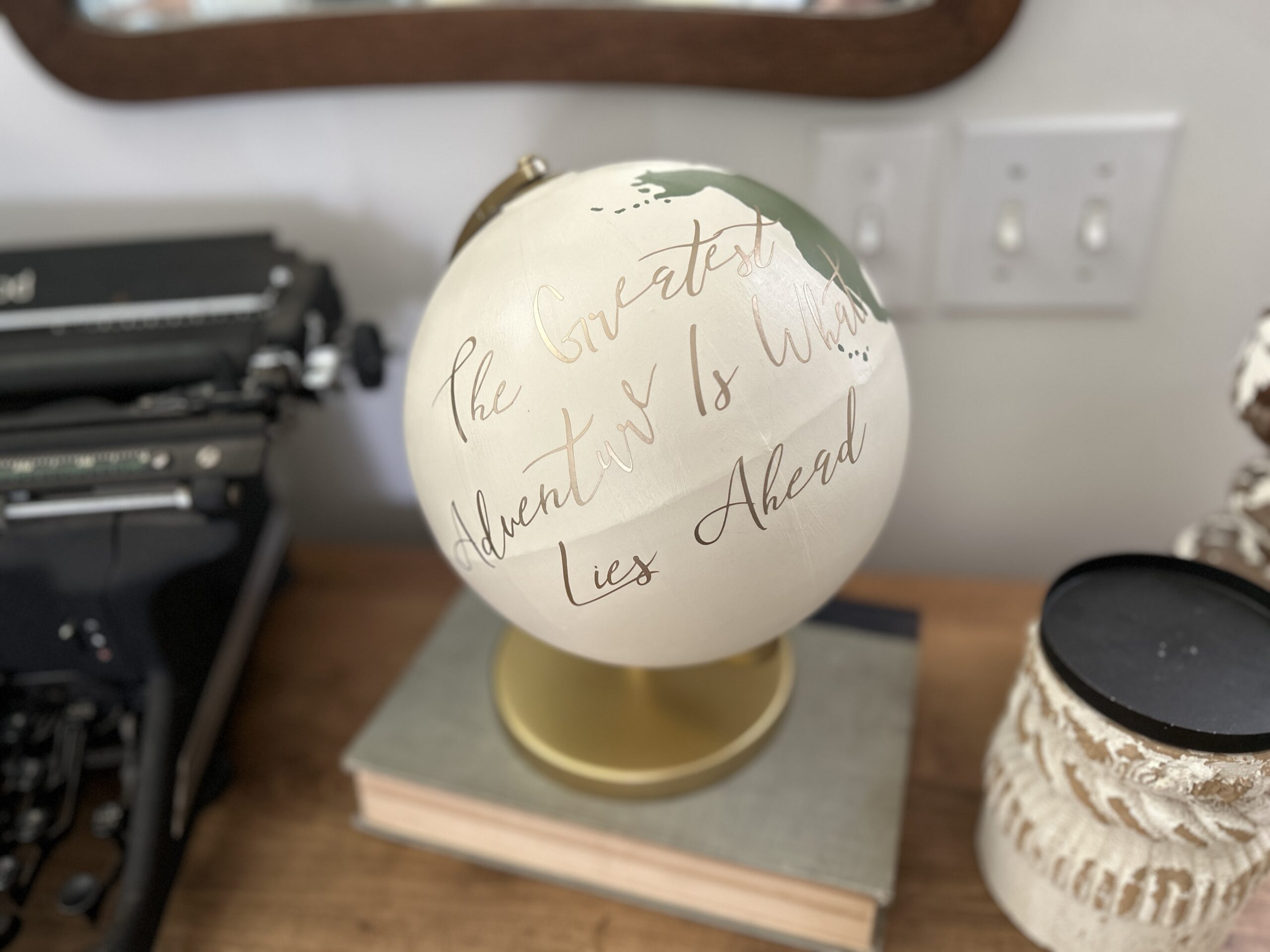 DIY painted globe turned into a guest book with gold vinyl lettering that says "the greatest adventure is what lies ahead"