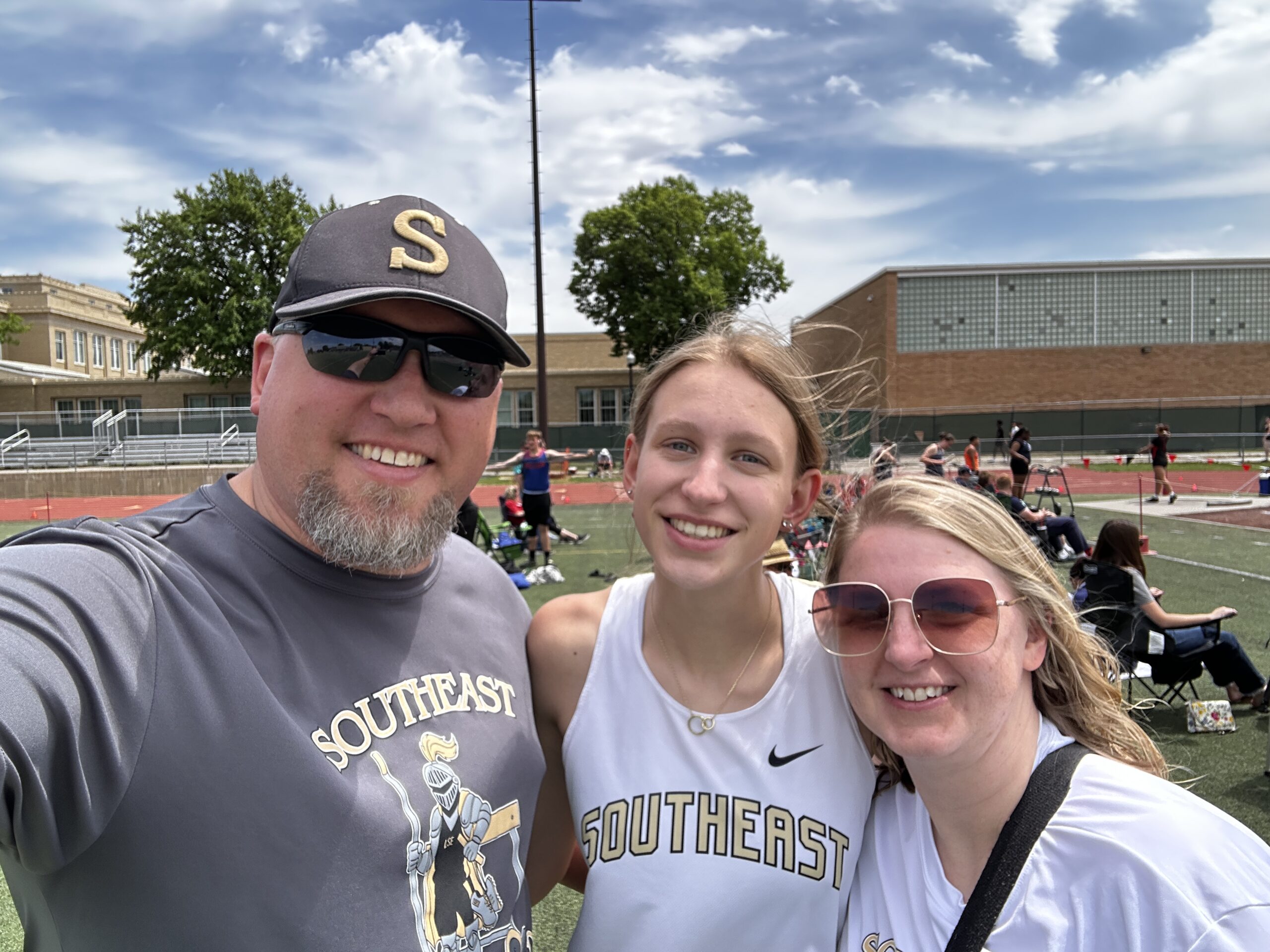 Parents standing with daugther and smiling taking a family selfie at the district track meet after her last time competing